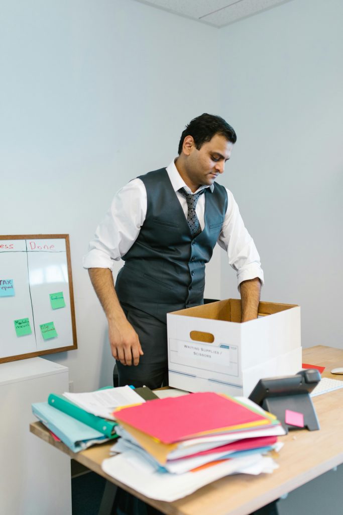 pexels photo 7581031 7581031 Professional man packing belongings into a box at an office desk, preparing to leave the workplace.